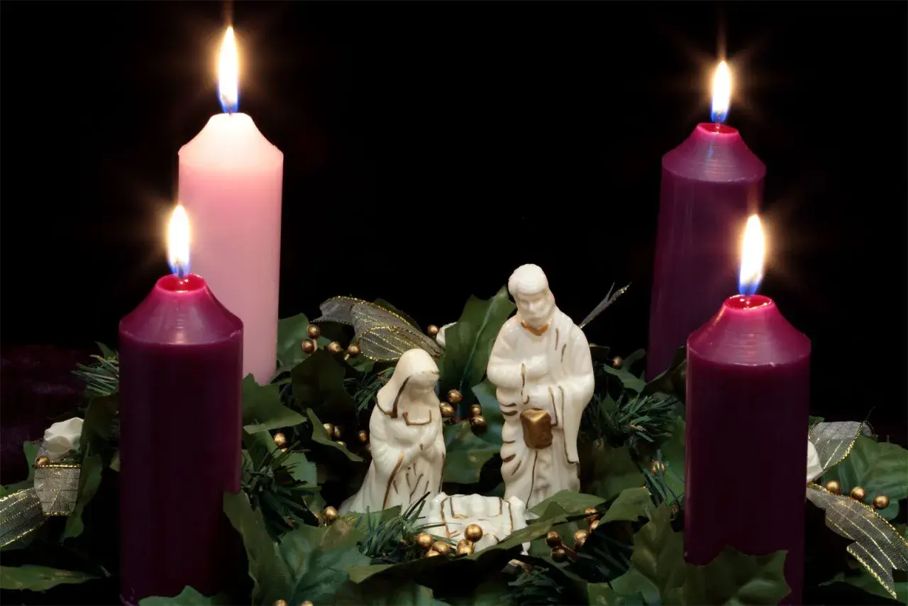 Three lit candles, two purple and one pink, surround a nativity scene. This is the advent 3rd Sunday.