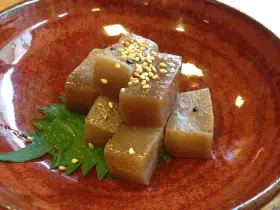 A simple dish of konjac jelly cubes, seasoned with sesame seeds and chili flakes, served on a green leaf in a rustic bowl. This is what monks eat.