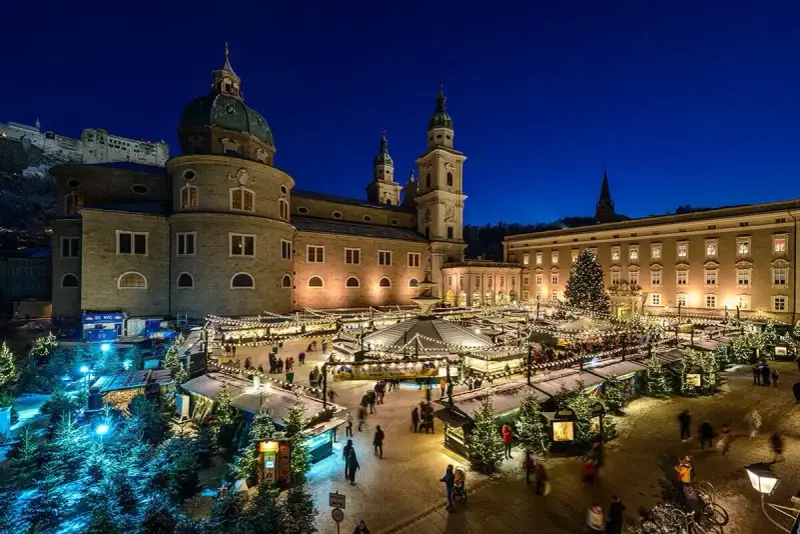 A magical Salzburg Austria Christmas market glows at night, with stalls, trees, and the cathedral creating a festive scene.