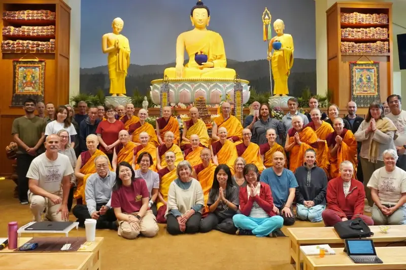 A large group of monks and laypeople gather for a photo in front of a golden Buddha statue, celebrating their shared religion.