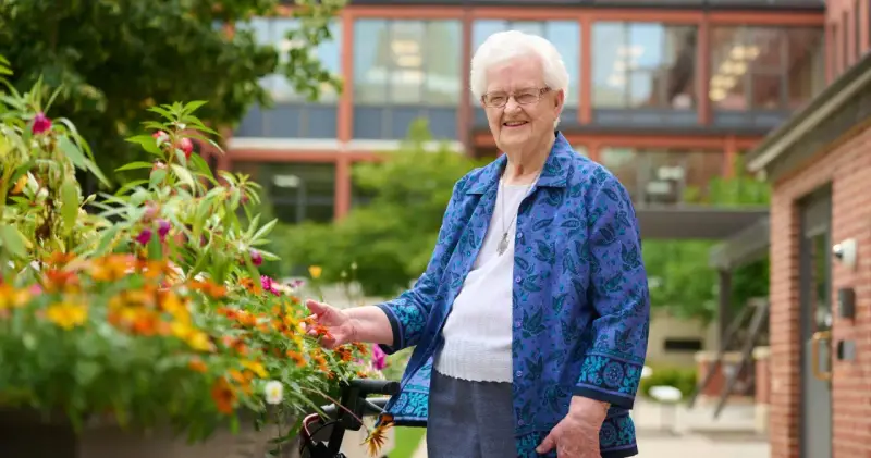 An elderly woman smiles, tending to flowers outside the St. Rose of Viterbo Convent.